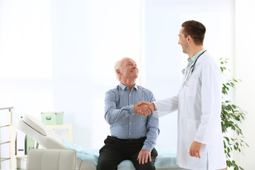 Doctor and elderly patient shaking hands in hospital. Space for text