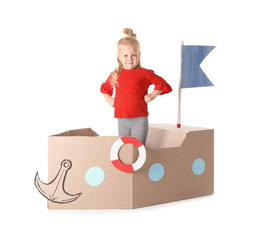 Cute little girl playing with cardboard ship on white background