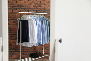 Reflection of wardrobe rack with men's clothes near brick wall in mirror at home. Space for text