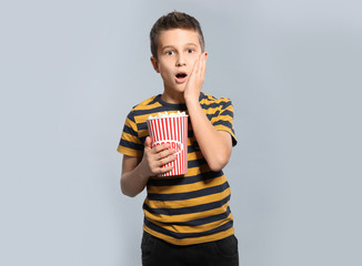 Fototapeta premium Emotional boy with popcorn during cinema show on grey background