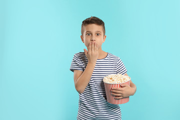 Emotional boy with popcorn during cinema show on color background