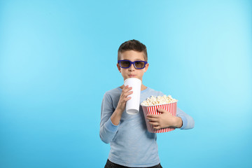 Boy with 3D glasses, popcorn and beverage during cinema show on color background