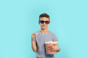 Boy with 3D glasses and popcorn during cinema show on color background