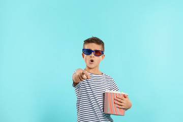 Emotional boy with 3D glasses and popcorn during cinema show on color background