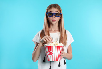 Emotional teenage girl with 3D glasses and popcorn during cinema show on color background