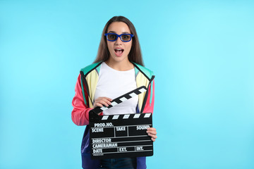 Emotional woman with 3D glasses and clapperboard on color background. Cinema show