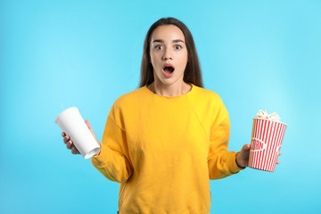 Emotional woman with popcorn and beverage during cinema show on color background
