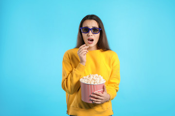 Emotional woman with 3D glasses and popcorn during cinema show on color background