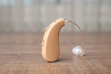 Hearing aid on wooden table, closeup. Medical device