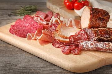Cutting board with different meat delicacies on wooden table