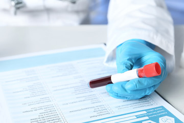 Specialist holding sample tube near laboratory test form medical on table, closeup. Research and analysis