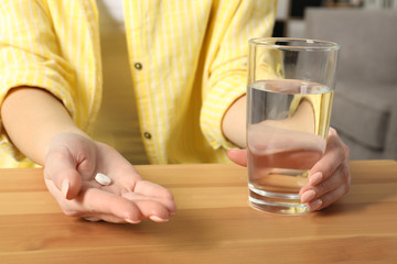 Woman with pill and glass of water at table, closeup