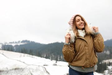Young woman in warm clothes near snowy hill, space for text. Winter vacation