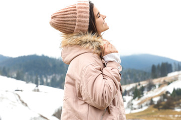 Fototapeta na wymiar Young woman in warm clothes near snowy hill. Winter vacation