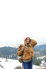 Young woman in warm clothes near snowy hill. Winter vacation