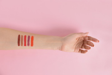 Woman with lipstick swatches on color background, closeup of hand