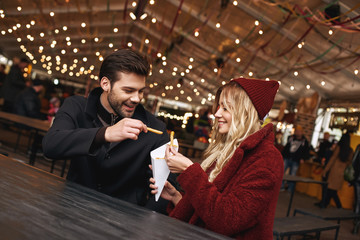 Close-up of young couple are eating french fries at the street food market.