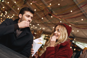 Close-up of young couple are eating french fries at the street food market.