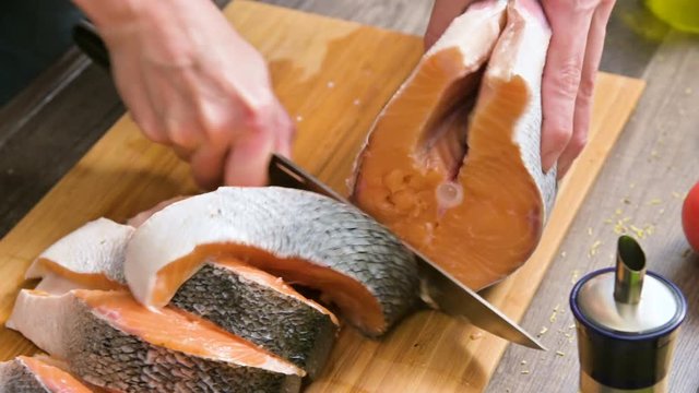 Close-up of female hands are cutting with a knife a large salmon on a wooden table of home cooking