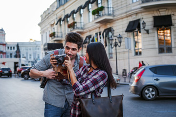 Young mixed race tourist couple watching on vintage camera while walking through the city