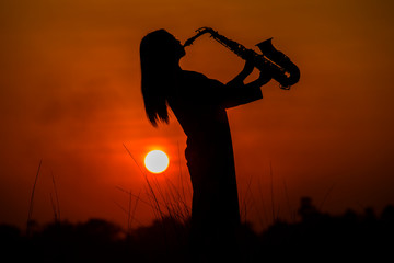 Silhouette of musician with saxophone sunset field,Saxophonist. woman playing on saxophone against...