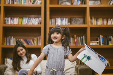 Cute little girl painting a picture with mother and show her work at home