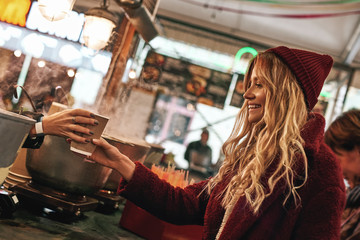Close-up of woman buying mulled wine at the street food market.
