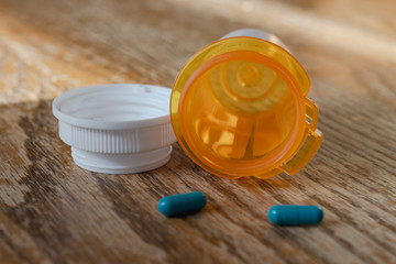 Prescription pill bottle with last two blue pills spilling onto wooden kitchen table.  Close up view.