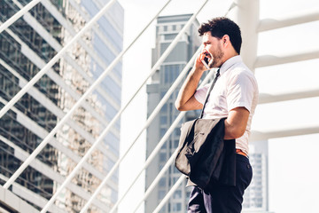 Fototapeta premium Portrait of handsome businessman in black suit standing and using smartphone outdoors on modern city background.man working with technology devices concept