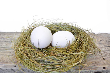 Two chicken eggs in a straw nest with text happy easter on rough wooden board on white background. Isolated