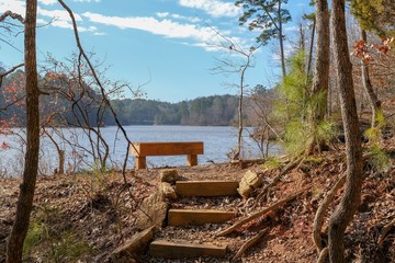 Fototapeta na wymiar A nicely located bench along a trail by Falls Lake at Blue Jay Point County Park in Raleigh, North Carolina. Great spot to sit and ponder.