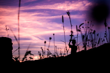 Children holding christian cross overhead with light sunset and behind tall grass,christian concept.