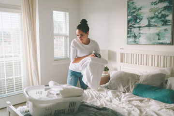 A woman folding laundry in a bright white bedroom.