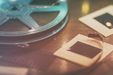Photo slides, film negatives and 8mm or super 8 vintage film reel on a wood table with soft lights.