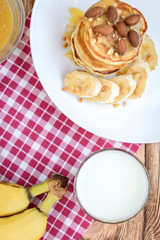 Pancakes with banana,nuts and honey on white plate for breakfast on wooden background with copy space.