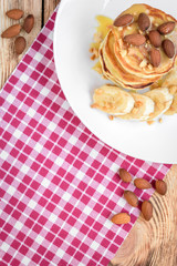 Pancakes with banana,nuts and honey on white plate for breakfast on wooden background with copy space.