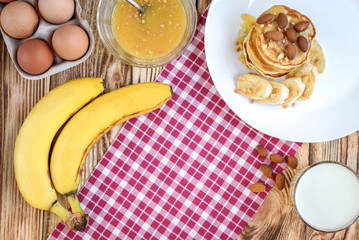 Pancakes with banana,nuts and honey on white plate for breakfast on wooden background with copy space.