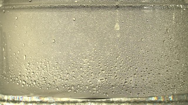 Drops of pure water or alcohol drip inside a glass jar, on silver background. The distillation process or the production of alcohol. Close-up