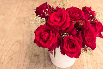 Red roses in a vase on a wooden floor