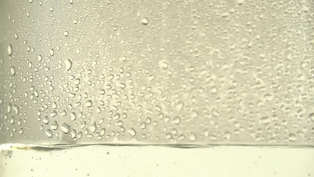 Drops of pure water or alcohol drip inside a glass jar, on white background. Focus shifts. The distillation process or the production of alcohol. Close-up