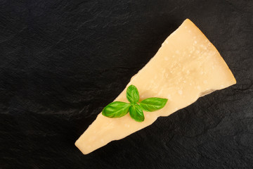 Aged Parmesan cheese, shot from the top on a black background with fresh basil leaves and a place for text