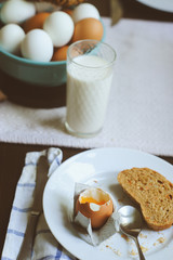 country breakfast on rustic home kitchen with farm eggs, butter, wholegrain bread and milk. Organic homemade food, easter concept.