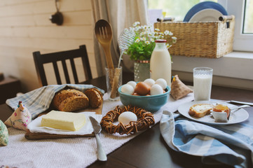 country breakfast on rustic home kitchen with farm eggs, butter, wholegrain bread and milk. Organic homemade food, easter concept.