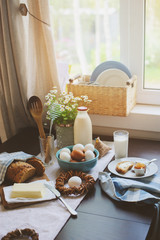 country breakfast on rustic home kitchen with farm eggs, butter, wholegrain bread and milk. Organic homemade food, easter concept.