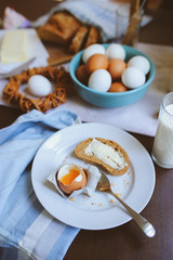 country breakfast on rustic home kitchen with farm eggs, butter, wholegrain bread and milk. Organic homemade food, easter concept.