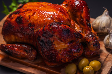 Whole roasted chicken on cutting board with vegetables over black background