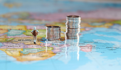 Miniature people standing on a map with two pile of coins. A concept of travel and cost.