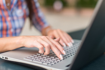 Young woman typing on a laptop keyboard working outdoors