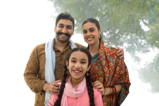 Portrait of a smiling village man standing with his wife and daughter posing for a family photo.	
