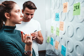 Intelligent coworking people preparing business strategy and posted on a sticky glass note wall. Manager team brainstorming on new business ideas